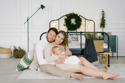 Happy family with a small child sitting on the floor next to the bed in the bedroom, decorated 