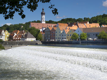 Houses by river and buildings against blue sky