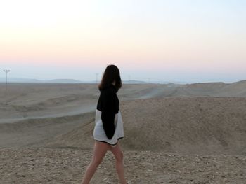 Woman standing on beach against sky during sunset