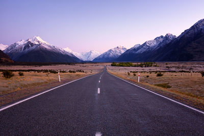 Road by snowcapped mountains against clear sky