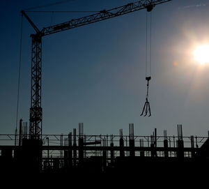 Silhouette cranes at construction site against sky during sunset