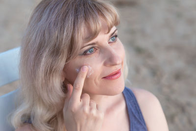 Close-up of beautiful mature woman applying cream while sitting on bench in park