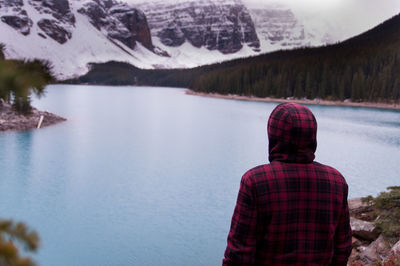 Rear view of man standing by lake against mountain