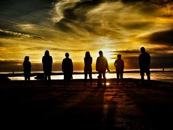 Silhouette people on beach against sky during sunset