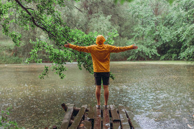 Full length of woman standing on tree by lake during rainy season