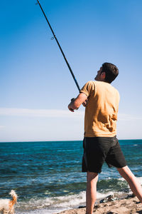 Rear view of man fishing in sea against sky