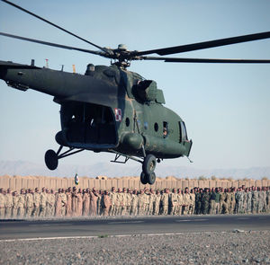 Helicopter flying against army soldiers standing on road