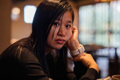 Close-up portrait of woman with hand on chin in cafe