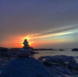 Silhouette rocks on beach against sky during sunset