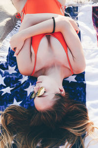 High angle view of young woman wearing sunglasses while lying on blanket at beach