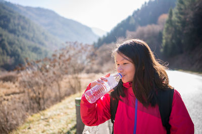 Beautiful young woman drinking water from while standing outdoors