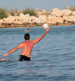 Rear view of shirtless man in sea against sky