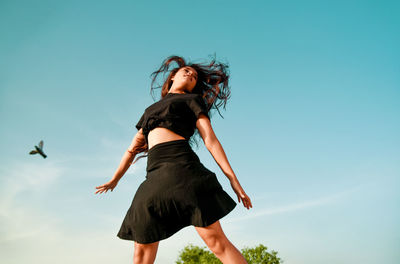 Low angle view of young woman dancing against blue sky
