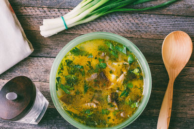 Mushroom soup in a bowl, bunch green onions, pepper mill and a wooden spoon on old wooden table