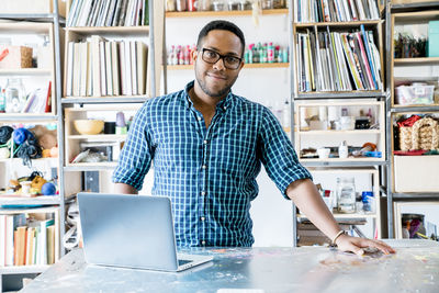 Portrait of confident businessman standing against racks while working in office