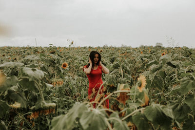 Young woman standing amidst sunflowers on field against sky