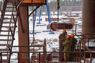 Pipes and cranes at snow covered construction site against sky