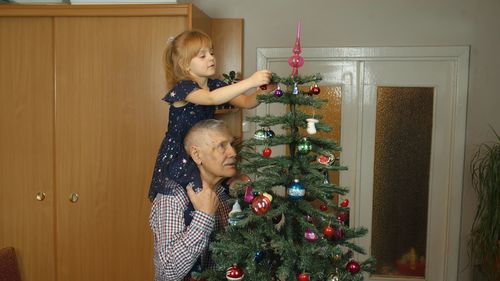 Granddaughter and grandfather decorating christmas tree at home