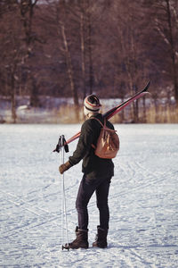 Rear view of male hiker carrying ski equipment on field