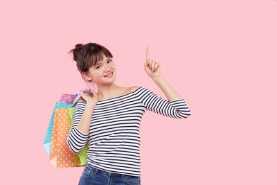 Smiling young woman standing against pink background