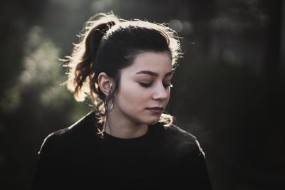 Young woman looking down against trees