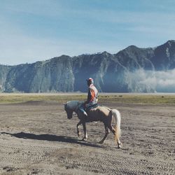 Full length of young woman riding horse on mountain