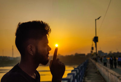 Optical illusion of man holding sun at bridge during sunset