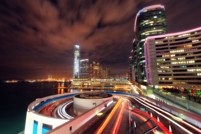 Light trails on illuminated buildings in city against sky at night