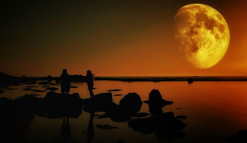 Silhouette people on calm beach against the moon