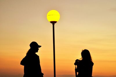 Silhouette women standing by street light against orange sky