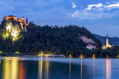Illuminated buildings by trees against sky