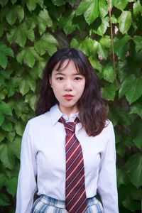 Portrait of a beautiful young woman standing against green leaves