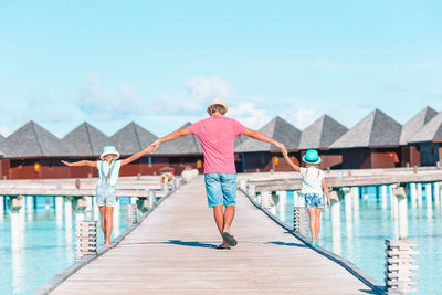 Rear view of father and daughters holding hands while walking on pier