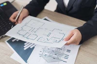 Midsection of businesswoman holding blueprint on table