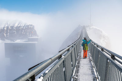 Rear view of girl walking on footbridge during winter