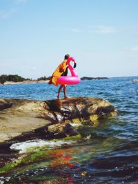 Side view of woman on rock by sea against sky