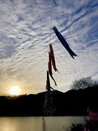 Silhouette flags hanging on lake against sky at sunset