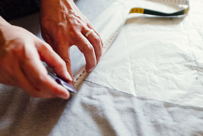 Cropped hands of tailor marking on white fabric on table