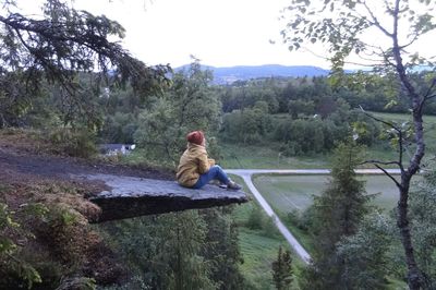 Rear view of woman sitting on riverbank in forest