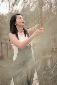 Young woman with arms raised standing against trees