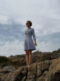 Young woman standing on rock against sky