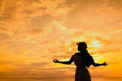 Silhouette woman standing against orange sky