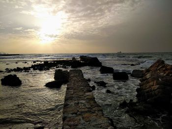 Rocks on beach against sky during sunset