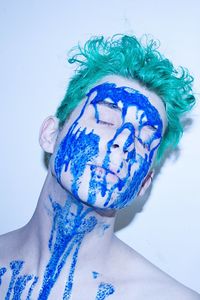 Close-up of man with blue face paint against white background