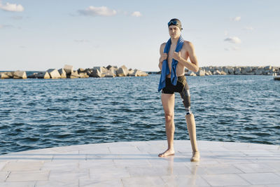 Disabled young man with towel around neck standing against sea on promenade