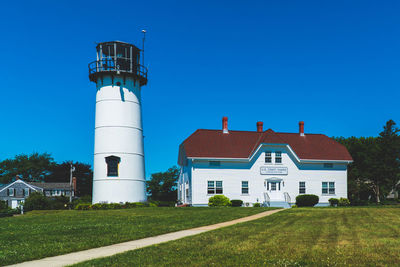 Lighthouse on field by building against clear blue sky