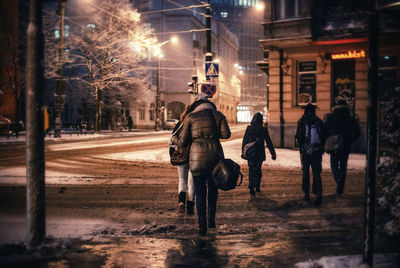 Rear view of people walking on city street at dusk during winter