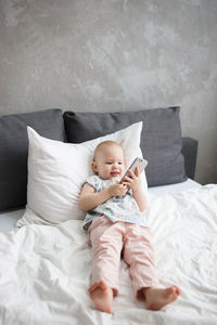 Baby girl with phone lies on pillow in white bed. alpha generation.