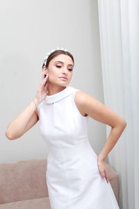 Indoor cropped  image of bride in white classic dress and bridal tiara, minimalist home interior