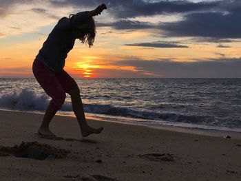 Silhouette woman standing on beach against sky during sunset